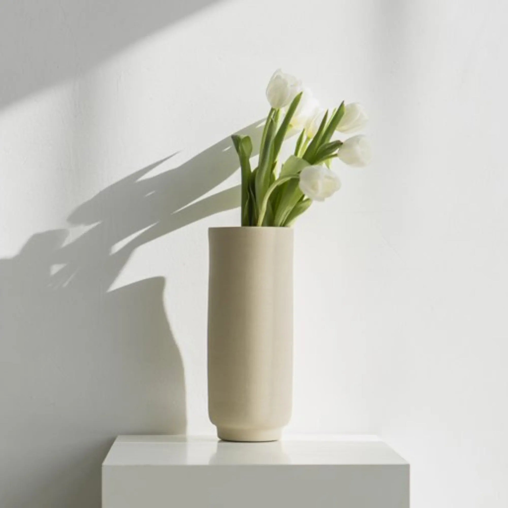 O Cactuu | Beige vaas Solvi met witte tulpen op een witte sokkel | Conceptstore Sisalla